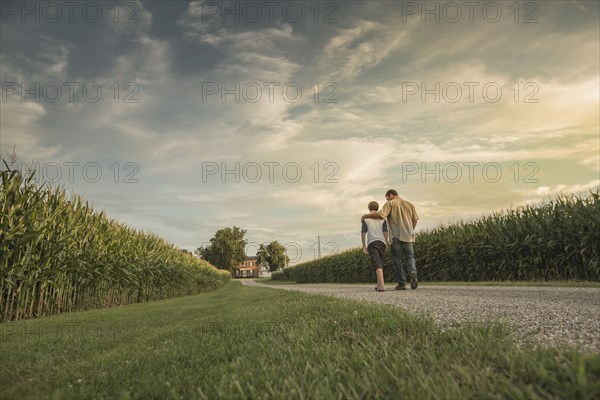 Caucasian father and son walking on dirt path by corn field