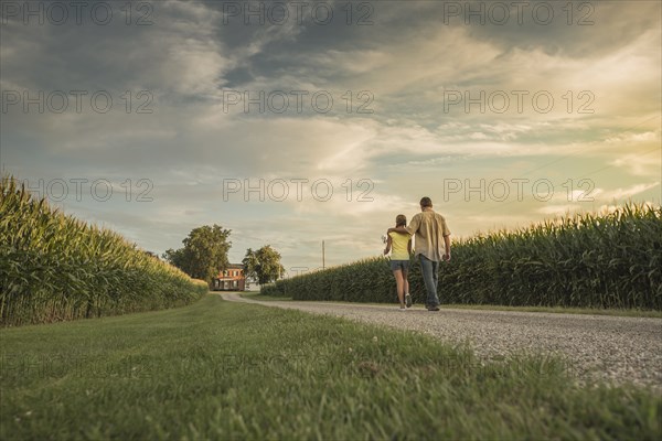 Caucasian father and daughter walking on dirt path by corn field