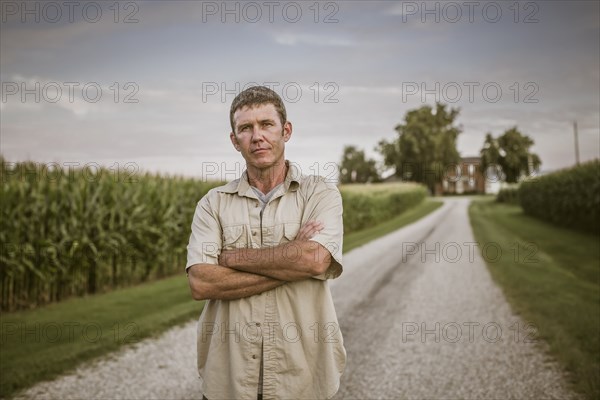 Caucasian farmer standing on dirt road by corn field