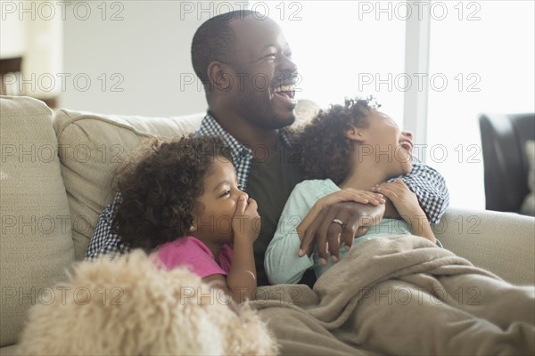 Father and daughters watching television on sofa