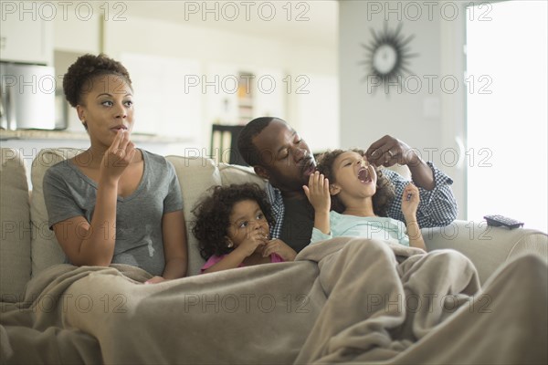 Family in blanket snacking on sofa