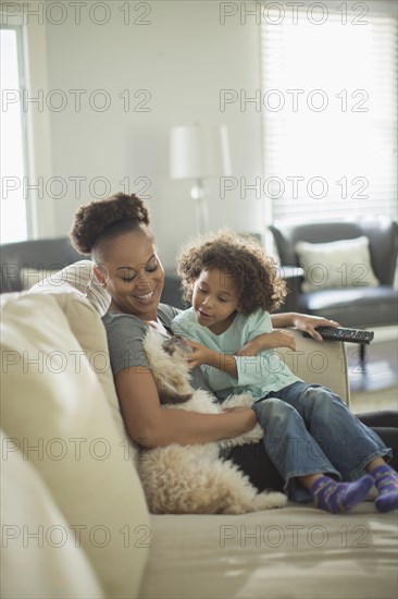 Mother and daughter petting dog on sofa