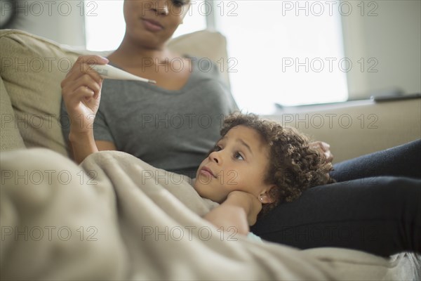 Mother measuring temperature of daughter on sofa