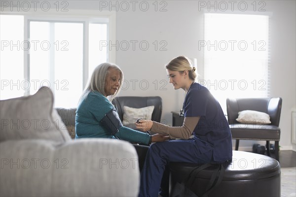 Nurse taking patient blood pressure in living room