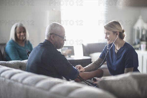 Nurse taking patient blood pressure in living room