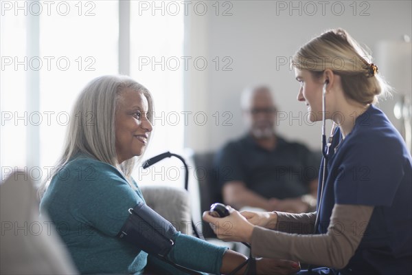 Nurse taking patient blood pressure in living room