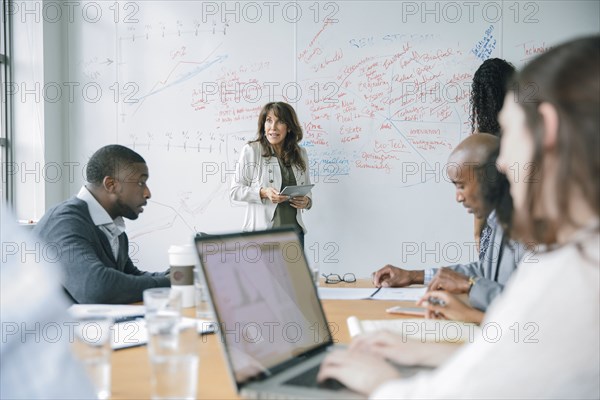 Businesswoman holding digital tablet near whiteboard in meeting