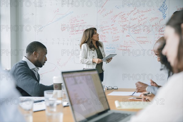 Businesswoman holding digital tablet near whiteboard in meeting