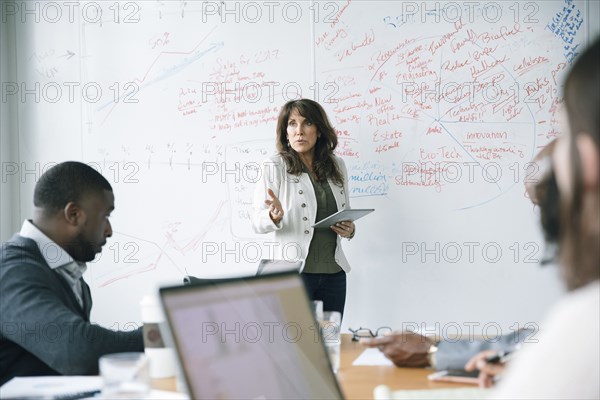 Businesswoman holding digital tablet near whiteboard in meeting