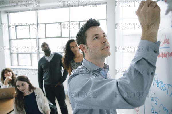 Businessman writing on whiteboard in meeting