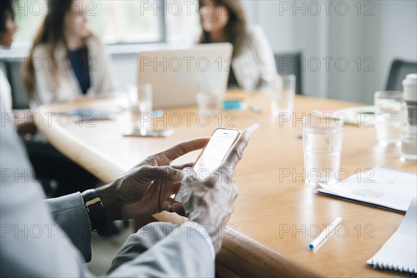 Businessman texting on cell phone in meeting