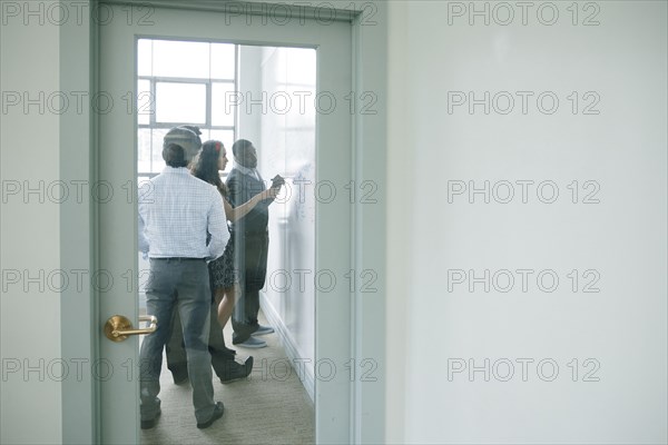 Businessman writing on whiteboard in meeting behind window