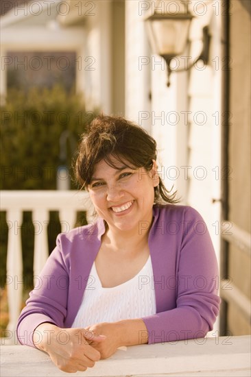 Hispanic woman leaning on porch railing