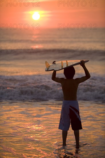 Asian boy holding surfboard at beach