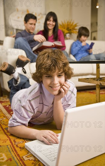 Hispanic boy looking at laptop with family in background