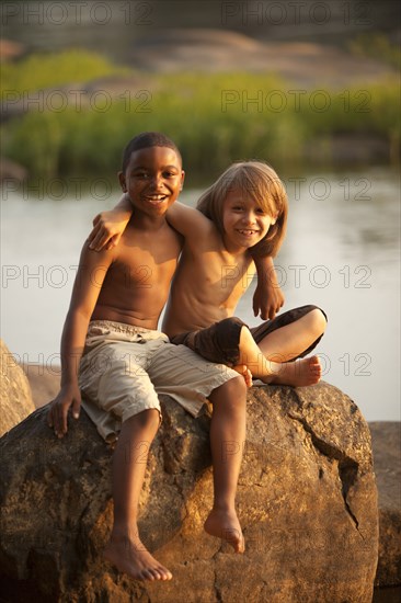 Smiling boys hugging on rock near lake