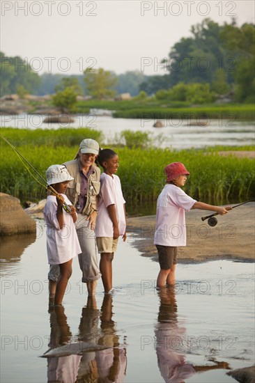 Woman teaching children how to fly fish on river