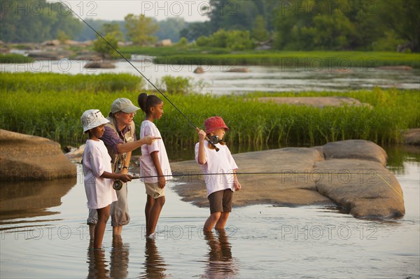 Woman teaching children how to fly fish on river