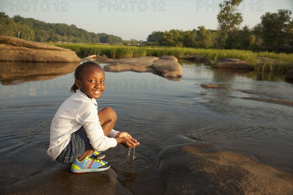 African American girl scooping water from river