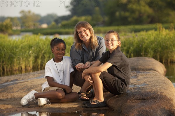 Teacher and students sitting on rock near river