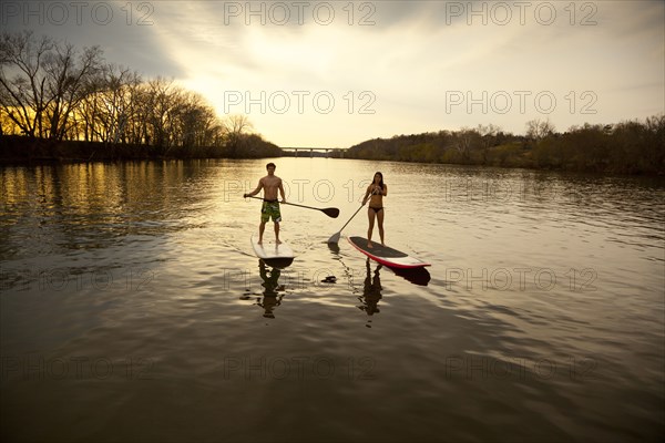 Couple paddling in river on surfboards