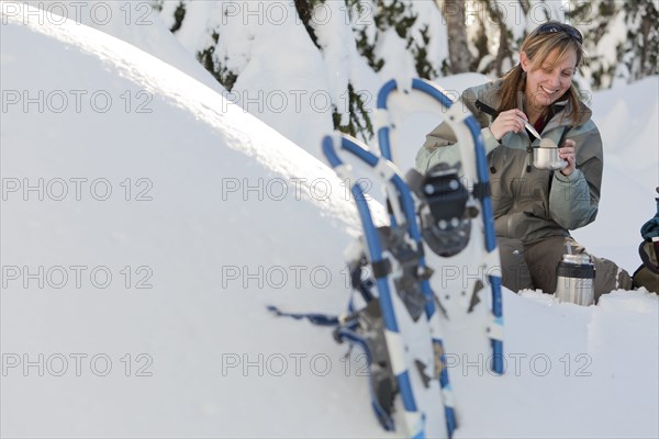 Caucasian woman with snowshoes eating in snow