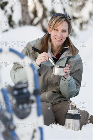 Caucasian woman with snowshoes eating in snow