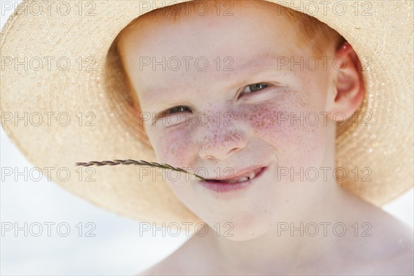 Freckled boy in hat chewing on straw