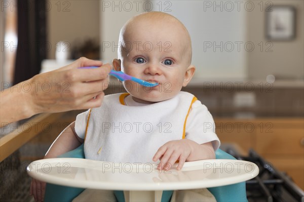 Caucasian mother feeding baby in high chair