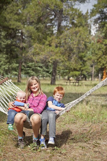 Caucasian children sitting in hammock outdoors