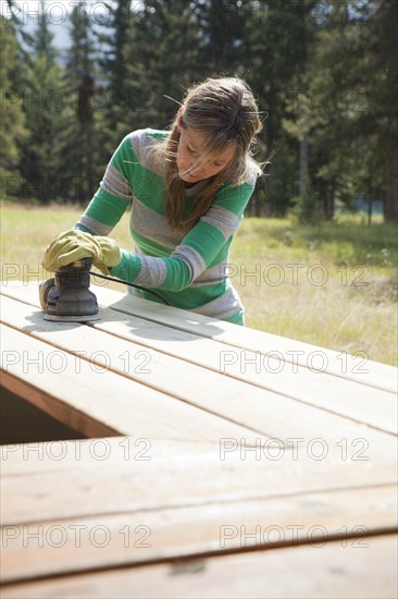 Caucasian woman sanding wood outdoors