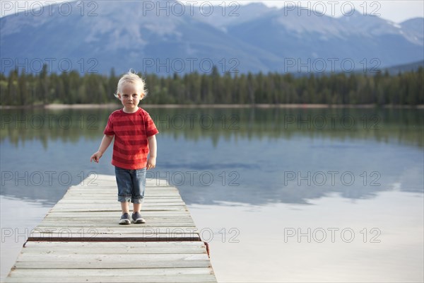 Caucasian boy walking on dock over remote lake