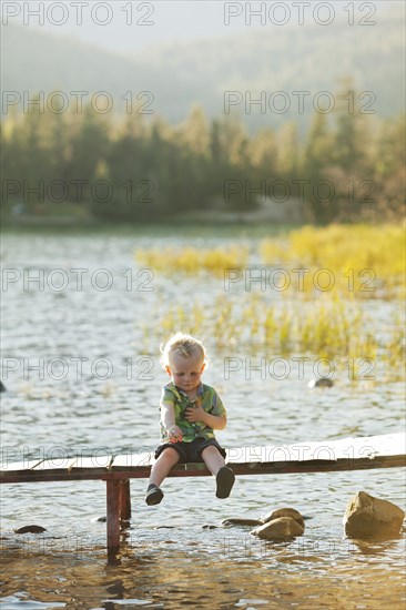 Caucasian boy sitting on wooden deck over lake