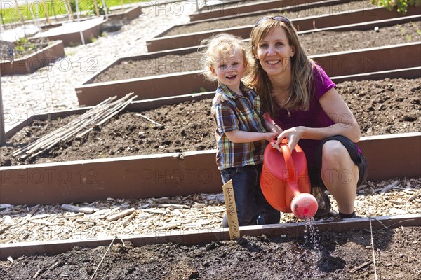 Caucasian mother and son watering plants in garden