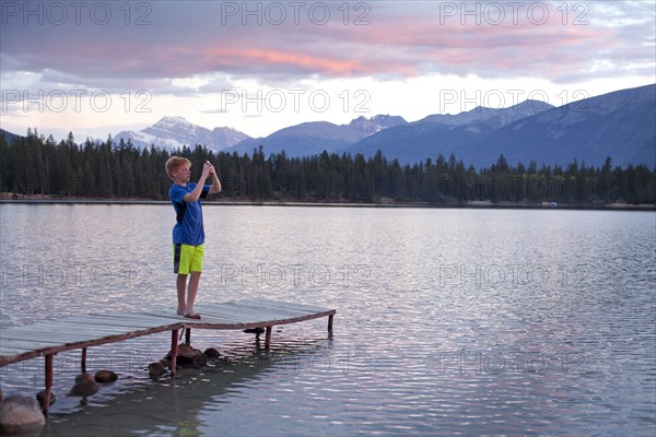 Caucasian boy standing on wooden dock photographing lake