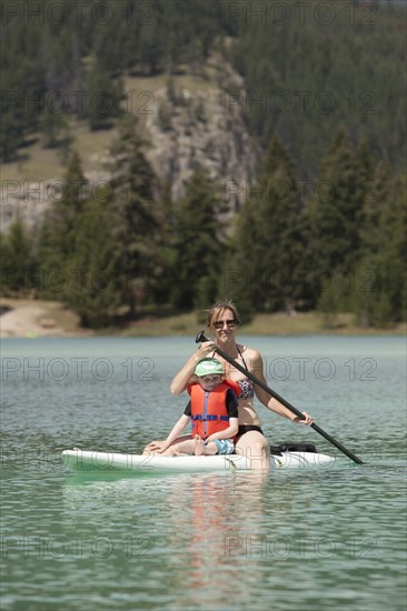 Caucasian mother and son sitting on paddleboard on lake
