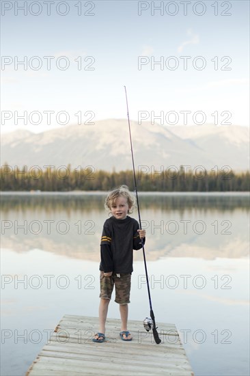 Caucasian boy standing on dock at lake holding fishing rod