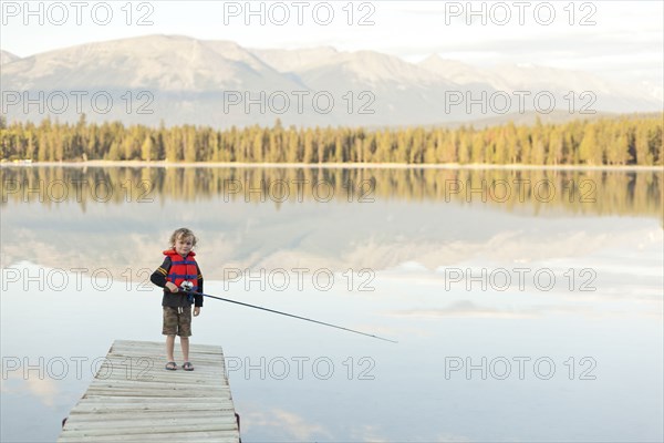 Caucasian boy standing on dock at lake holding fishing rod