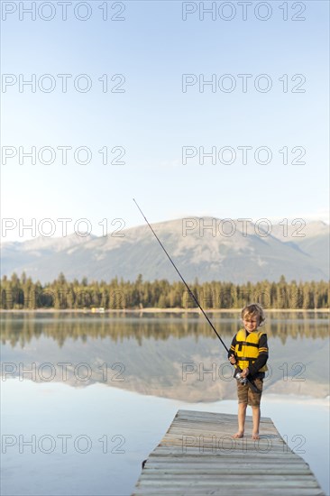 Caucasian boy standing on dock at lake holding fishing rod