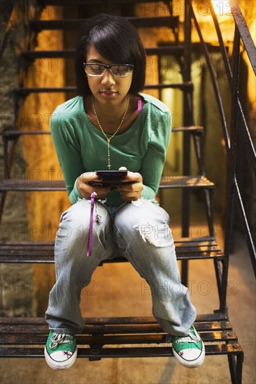 Hispanic girl text messaging on staircase