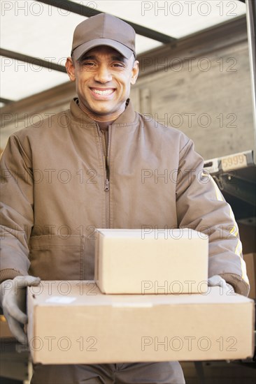 Smiling Hispanic delivery man carrying cardboard boxes