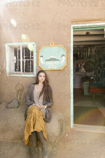 Hispanic teenage girl sitting near doorway to shop