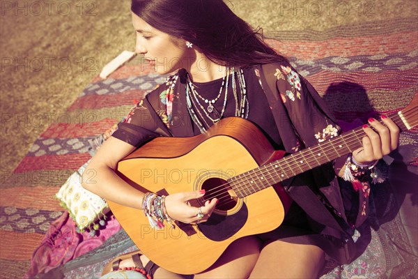 Asian woman sitting on blanket playing guitar