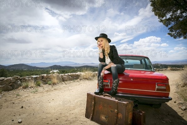 Caucasian woman sitting on trunk of car with suitcases