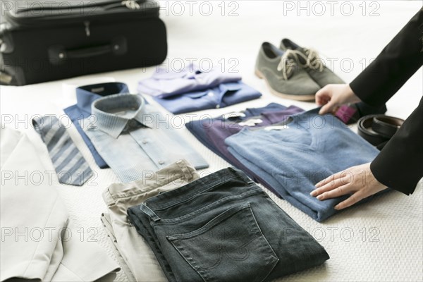 Hands of Caucasian woman arranging clothing for man on bed