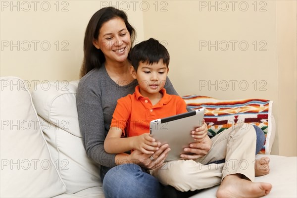 Son sitting in lap of mother using digital tablet