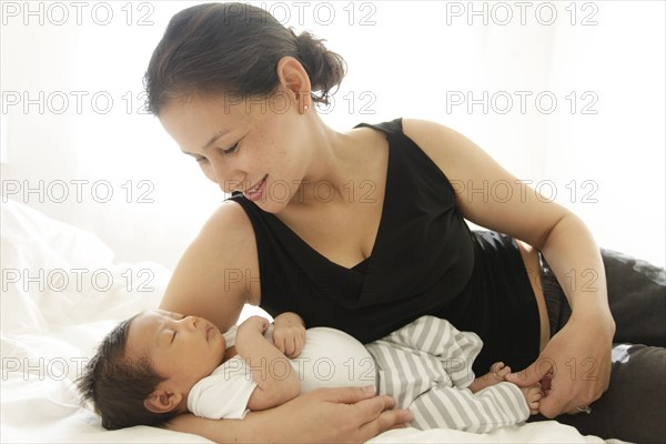 Mother laying on bed cradling sleeping baby son