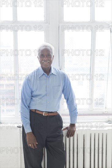 Smiling older Black man leaning on radiator near window