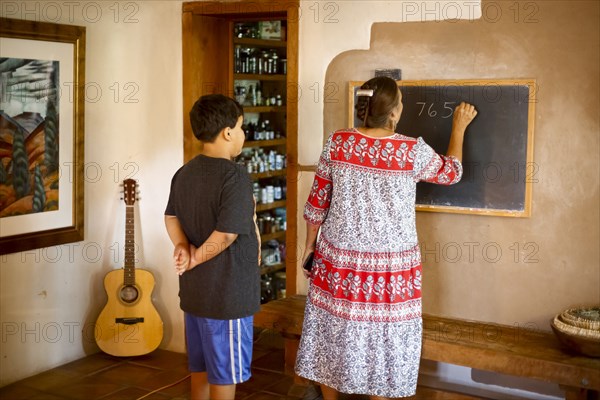 Woman writing equation on blackboard for son