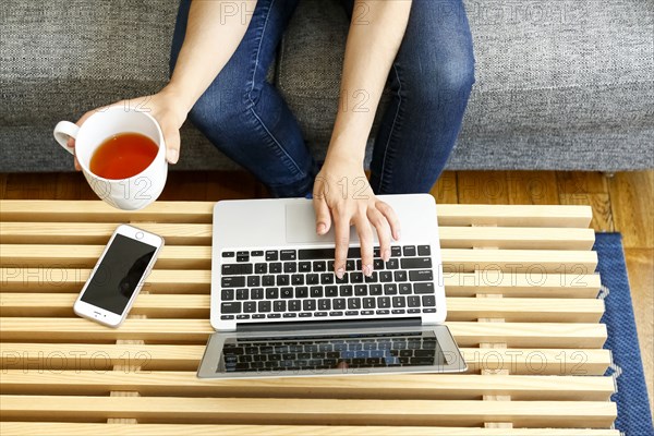Hands of mixed race woman using laptop and drinking tea